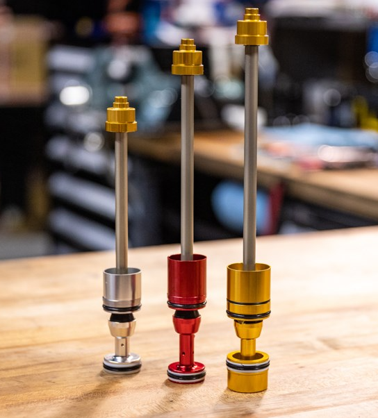 Three metal shock absorbers with gold, red, and yellow accents on a wooden surface.